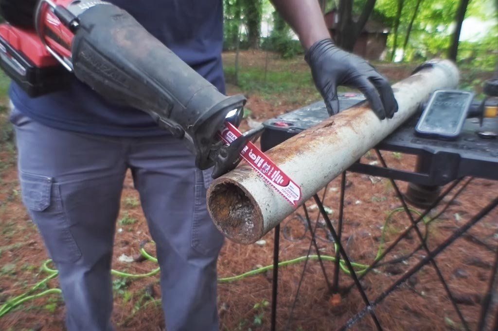 A man is cutting a pipe with a saw.