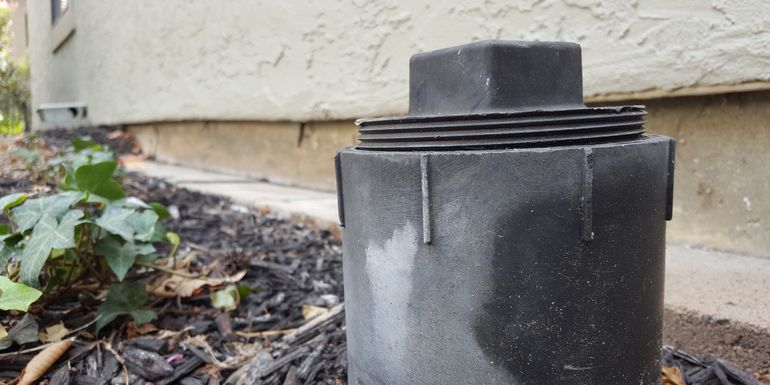 A black pipe is sitting in the dirt in front of a house.