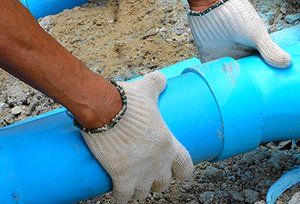 A man wearing white gloves is working on a blue pipe.