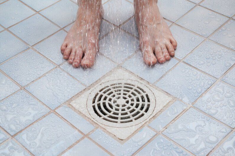A person is standing on a tiled floor next to a drain.