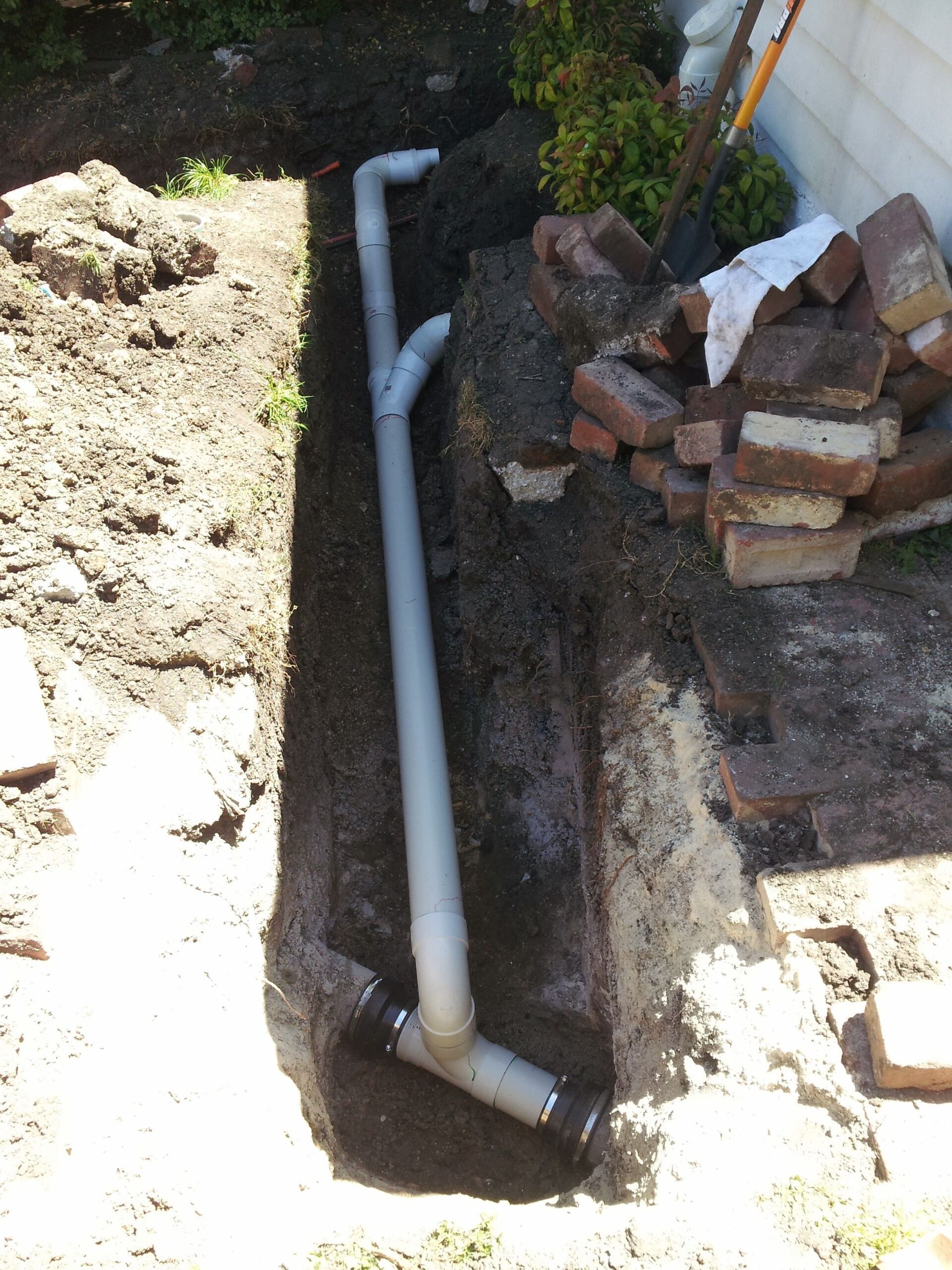 A white pipe is laying in the dirt next to a pile of bricks