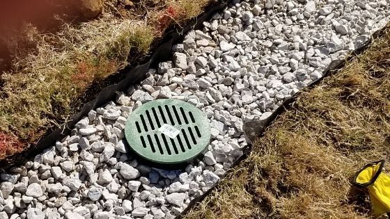 A green drain cover is sitting on top of a pile of gravel.