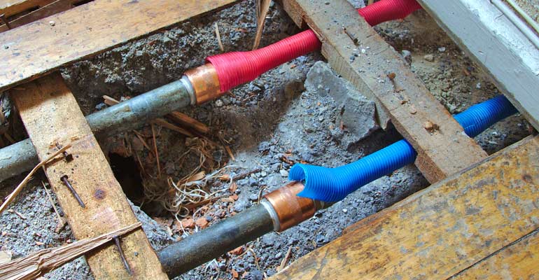 A bunch of pipes are laying on the ground under a wooden floor.