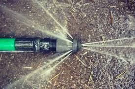 A green hose is spraying water into the ground.