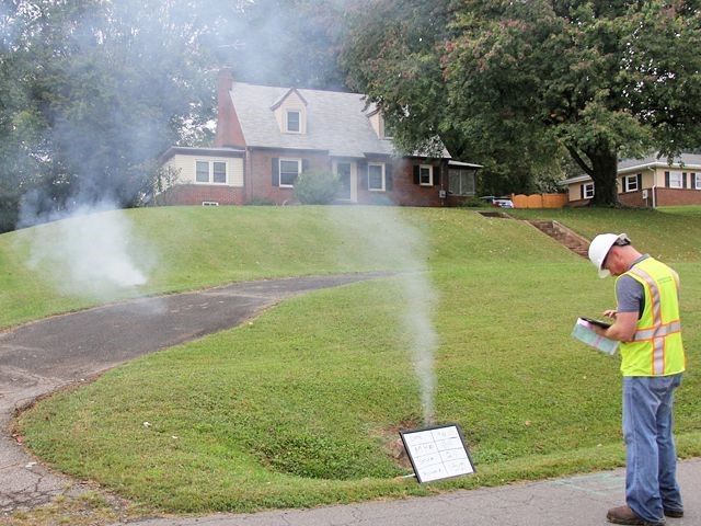 A man is standing in front of a house with smoke coming out of it.