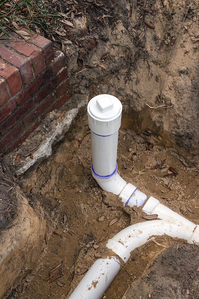 A replaced sewer pipe is sitting in the dirt next to a brick wall.