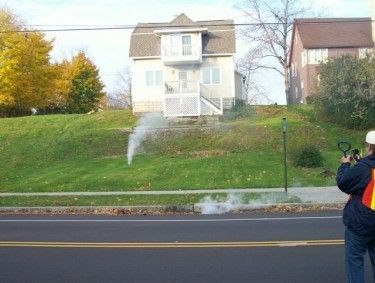 A man is taking a picture of a house with smoke coming out of it