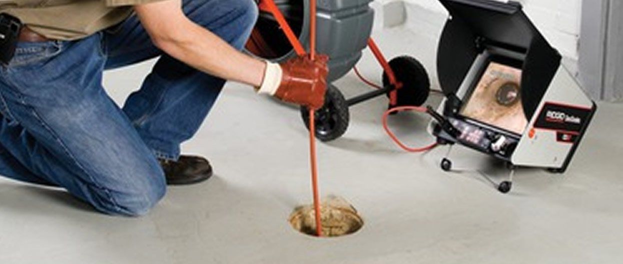 A man is kneeling down next to a camera and a hose.