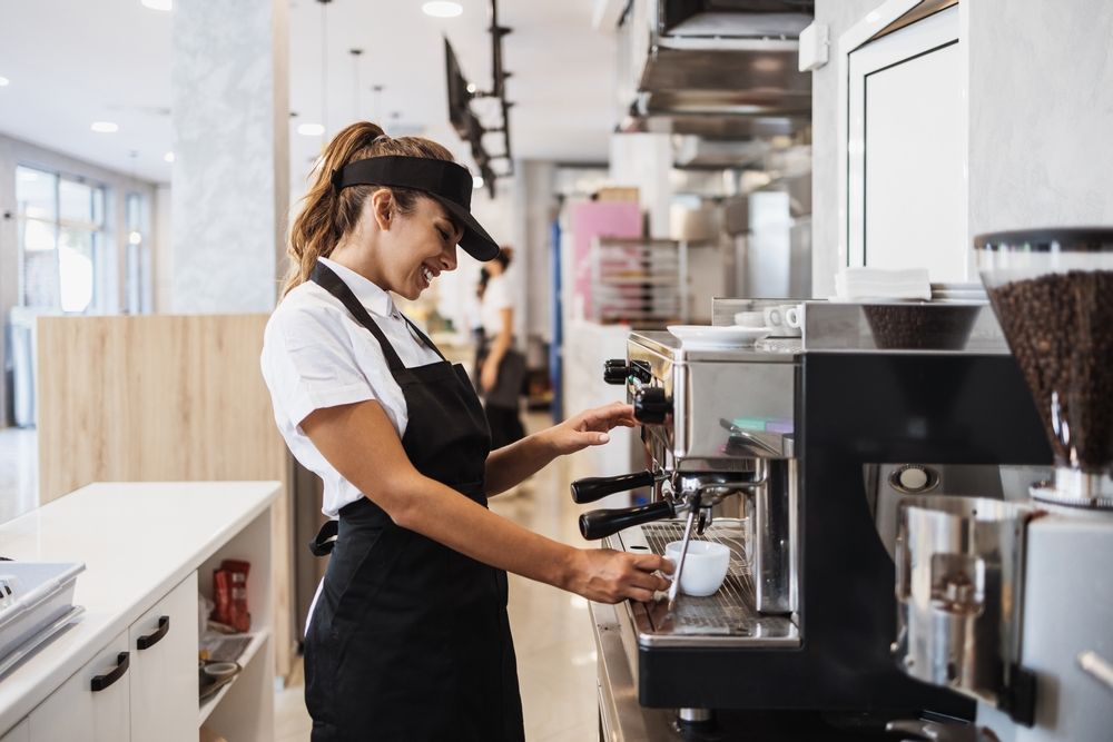 A woman is making a cup of coffee in a coffee shop.