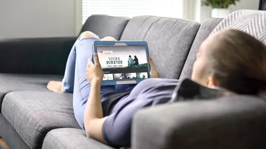 A woman is laying on a couch using a tablet computer.