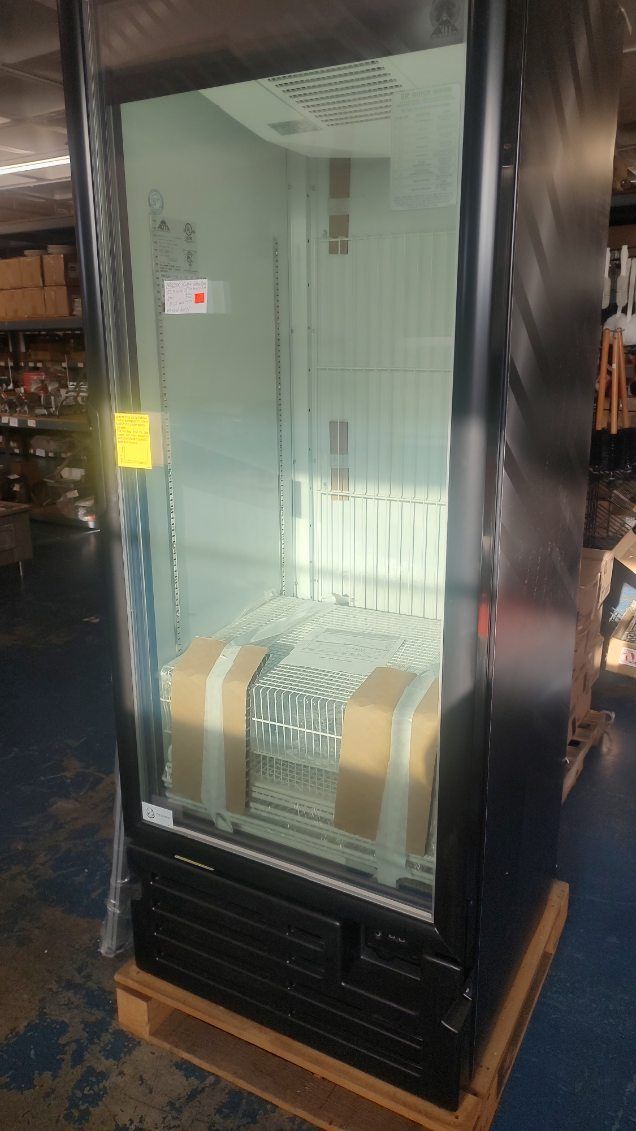 A black refrigerator with a glass door is sitting on a wooden pallet in a warehouse.