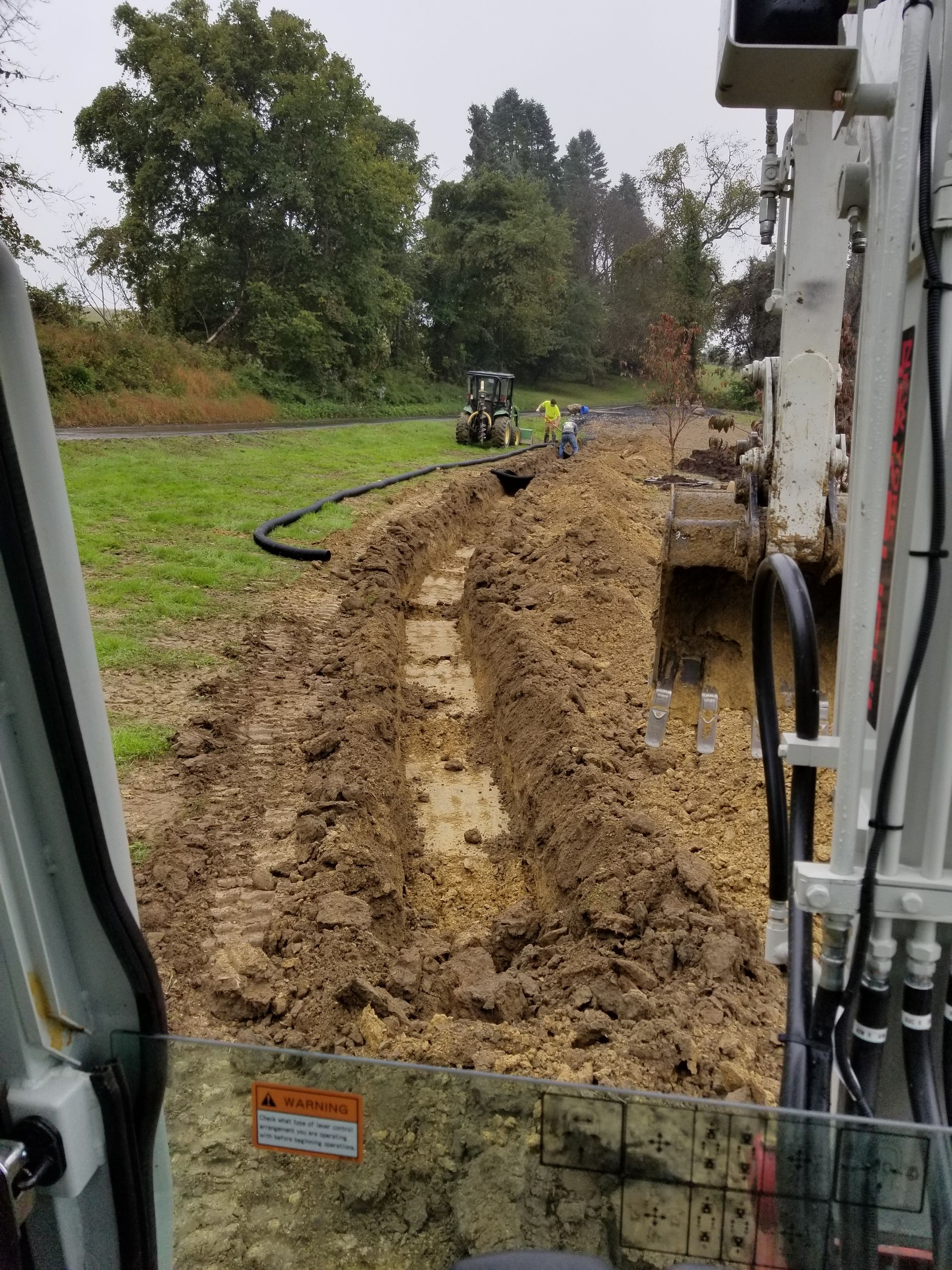 A white excavator is digging a hole in the dirt in a field.