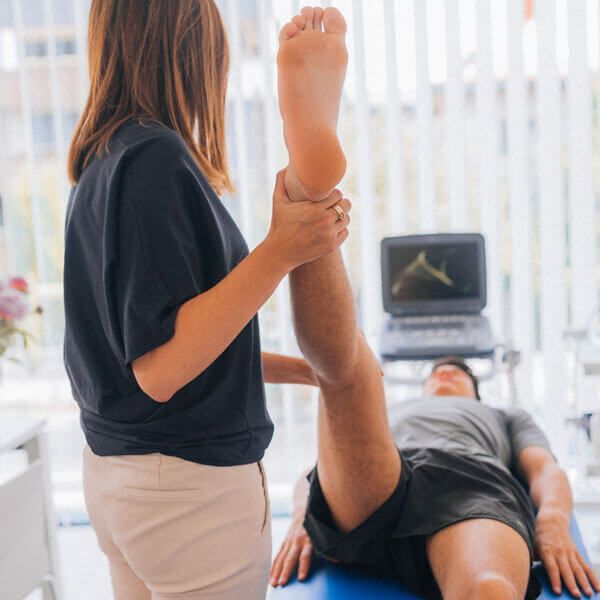 Physical therapist stretching a patient’s raised leg on a treatment table with a laptop nearby
