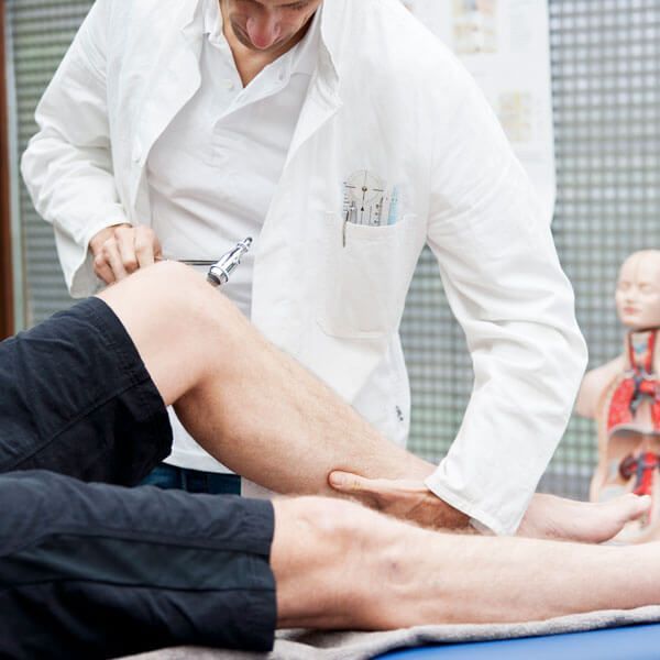 Doctor examining a patient’s knee during a medical exam, with anatomical model in the background
