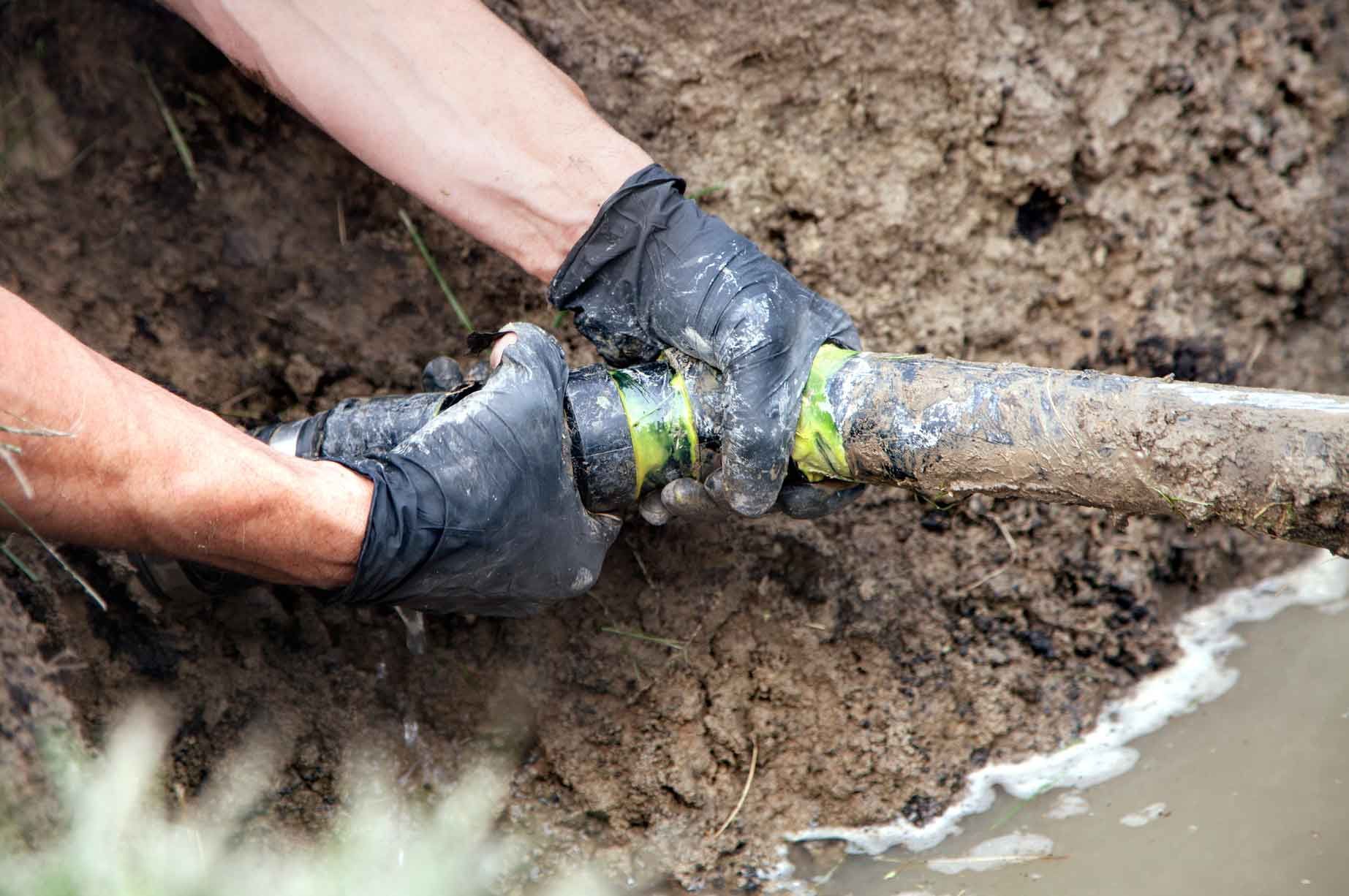 A person is fixing a pipe in the mud.