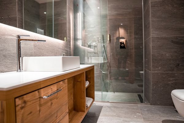 Interior of luxurious modern bathroom in resort Bathroom remodeling photo from a bathroom remodel project. Photo shows white sink on wooden cabinet with silver faucets and shower cabin with glass doors in a modern bathroom.