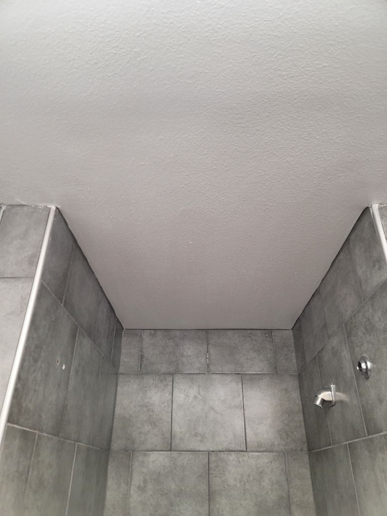 Looking up at a white textured ceiling inside a gray tiled shower stall.