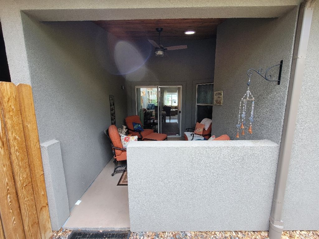 A covered patio with a textured gray wall, two orange chairs, a small table, and a ceiling fan viewed through an opening.