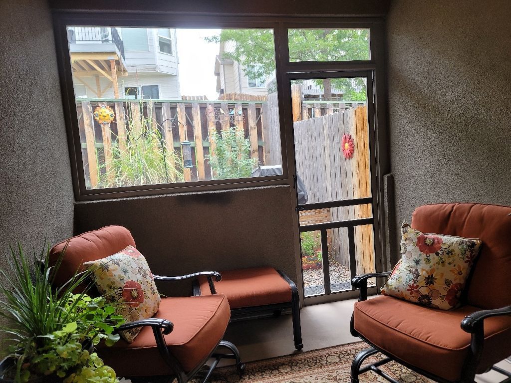 Two rust-orange armchairs with floral pillows face each other inside a screened-in porch with a garden view.