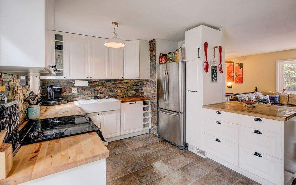 A modern kitchen with white cabinets, light wood countertops, a stainless steel refrigerator, and tiled backsplash.