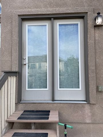 A light-colored double door with glass panels set in a stucco exterior wall above a short set of stairs.