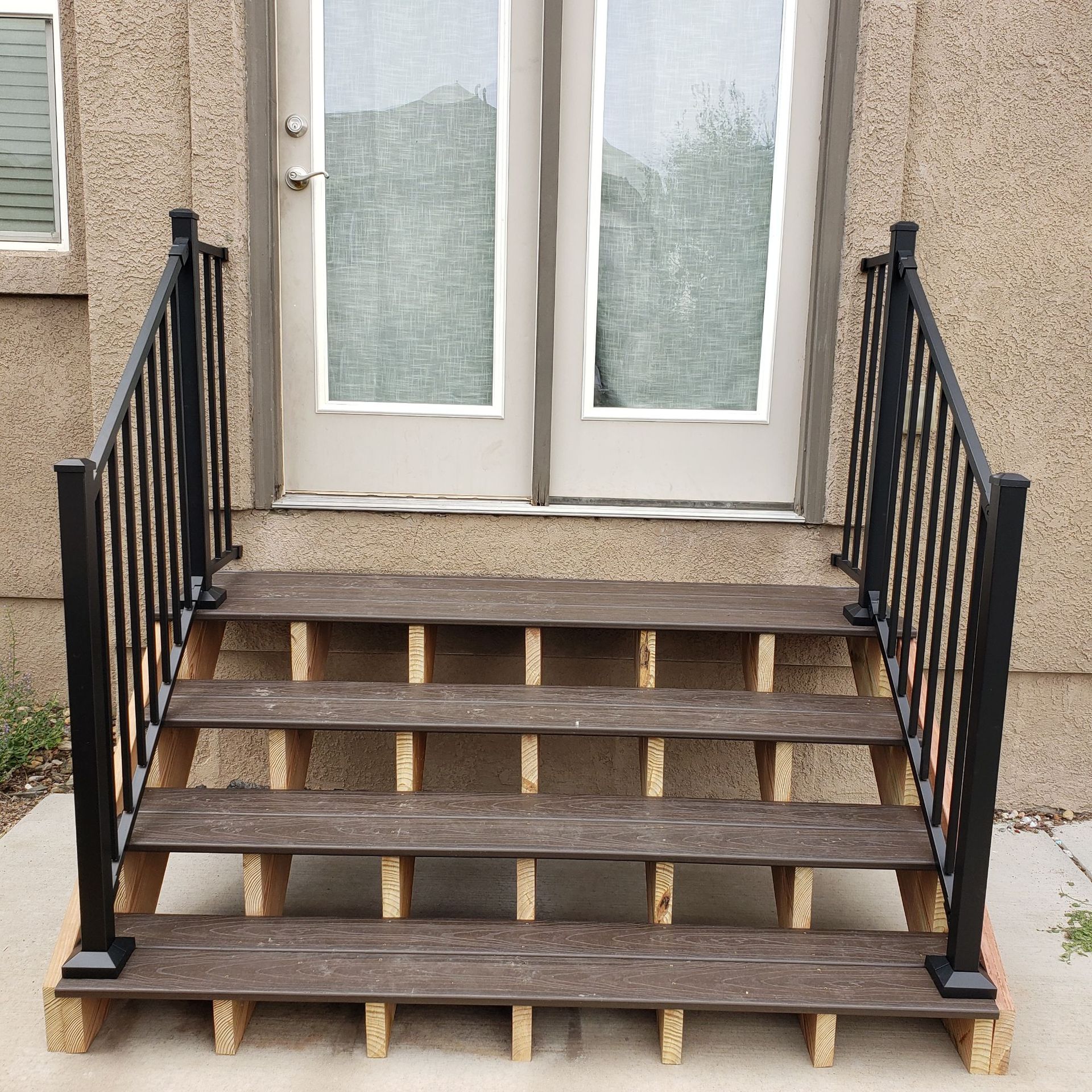 Wooden exterior stairs leading to double glass doors with black metal railings on both sides.