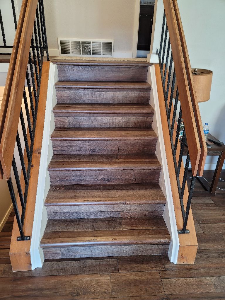Wooden staircase with dark brown treads and light wooden railings, featuring black metal spindles.