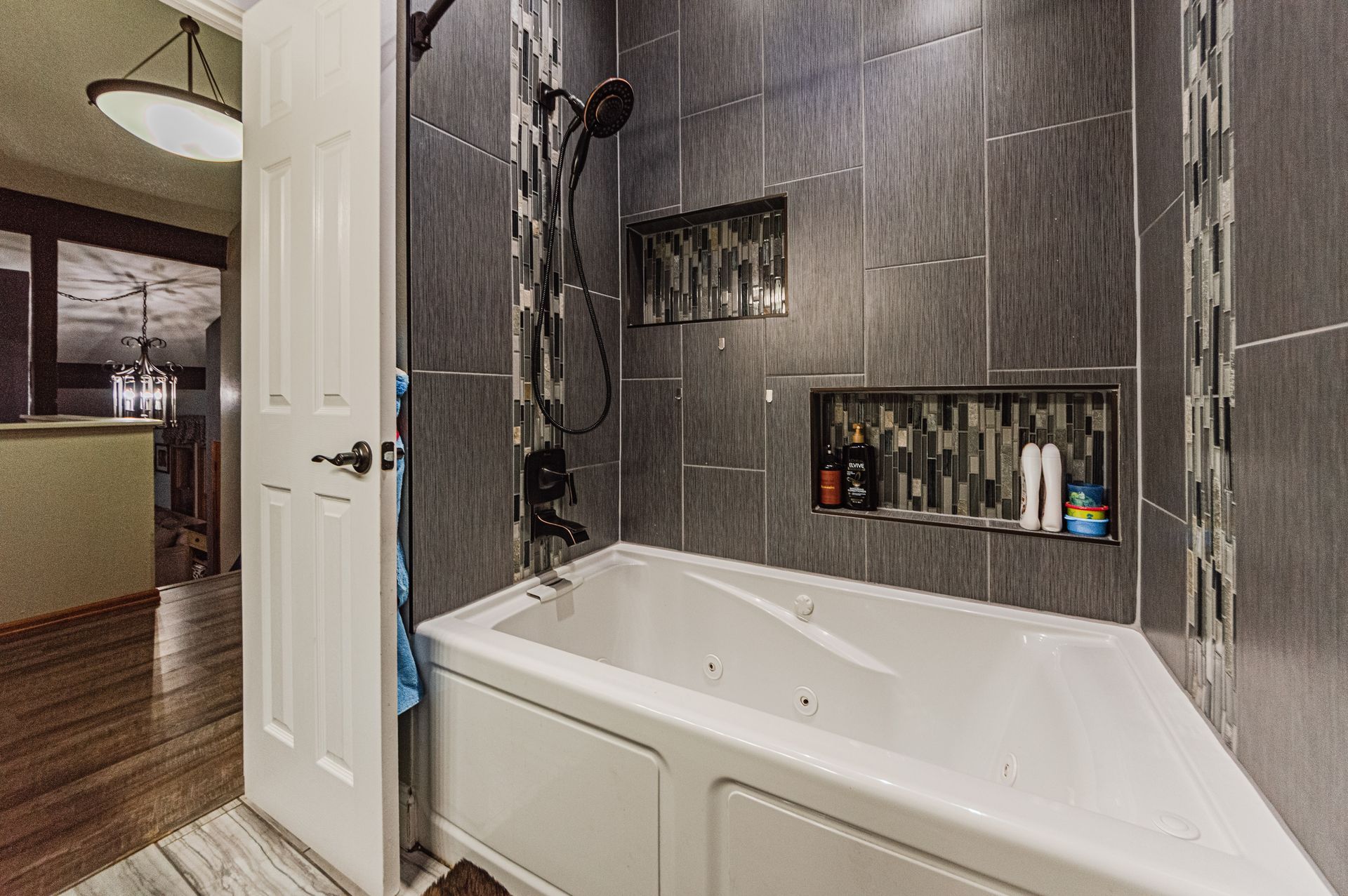 A modern bathroom featuring a white bathtub, gray tiled walls with vertical accents, and a built-in recessed niche.
