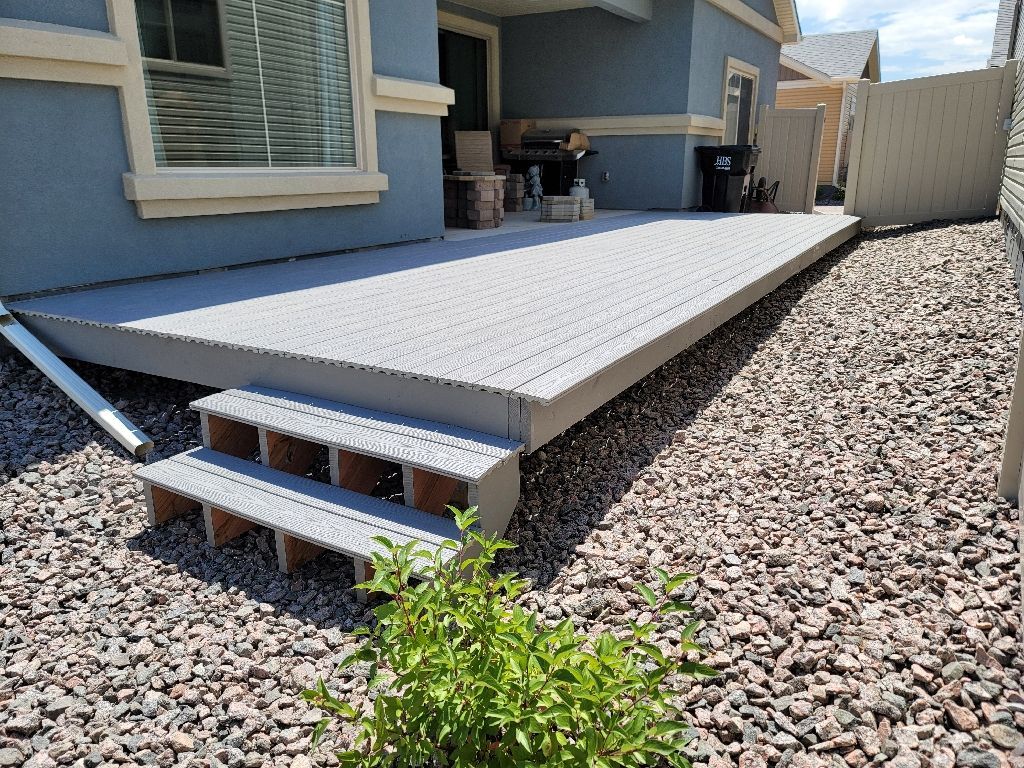 Light gray composite deck with two steps, set against a blue house exterior over a rock-covered backyard.