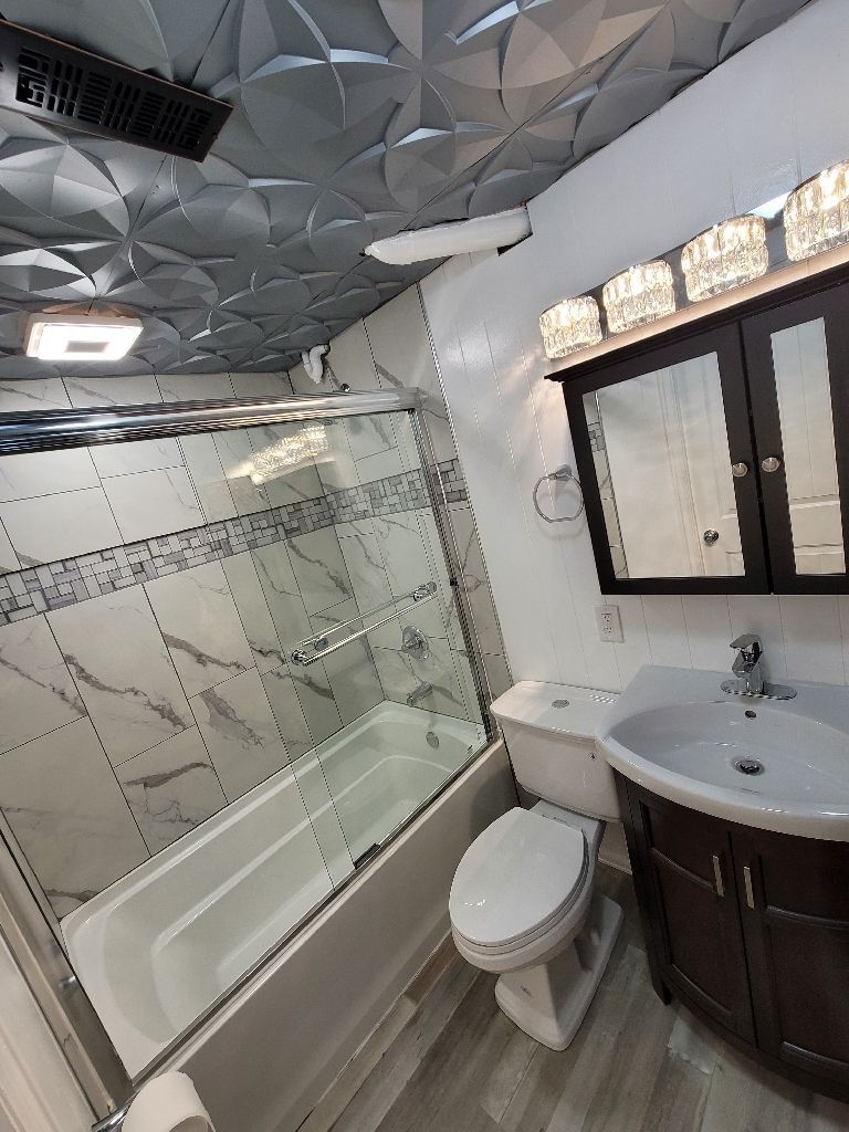 Bathroom with a patterned dark ceiling, marble-look tiled shower, white toilet, and dark vanity with a modern sink.