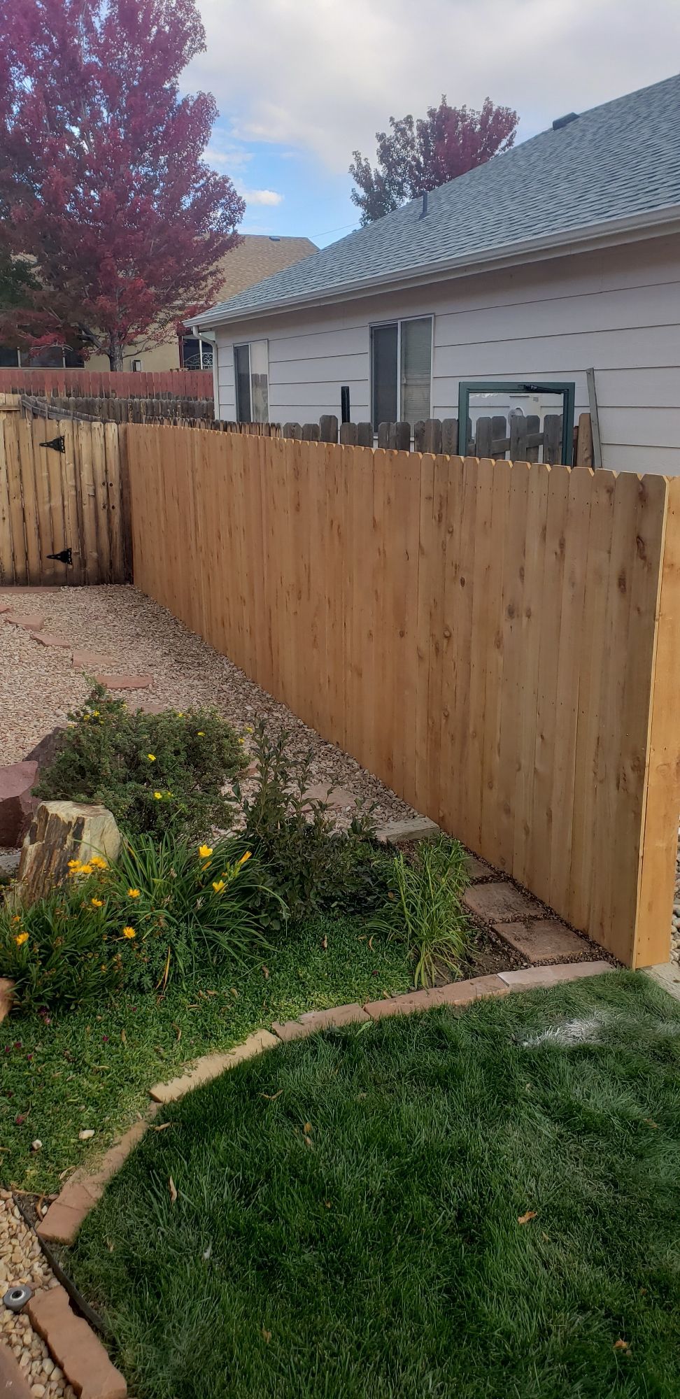 A newly installed wooden privacy fence lines a backyard, next to a house, gravel landscaping, and a small grassy area.