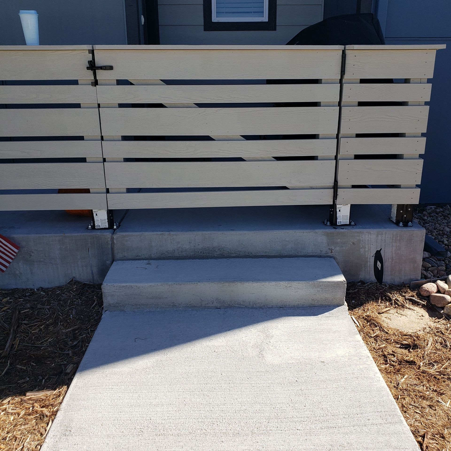 A wooden privacy fence made of horizontal slats surrounds a concrete patio entrance with a single step.