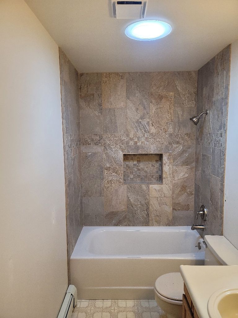 A bathroom featuring a white bathtub, a stone-tiled shower wall with a recessed niche, and a skylight in the ceiling.