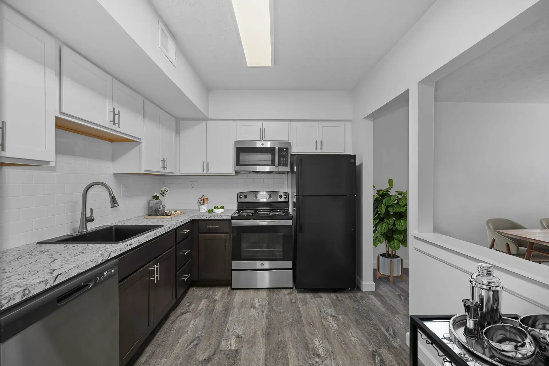 Modern apartment kitchen with white upper cabinets, dark lower cabinets, granite countertops, and stainless steel appliances.