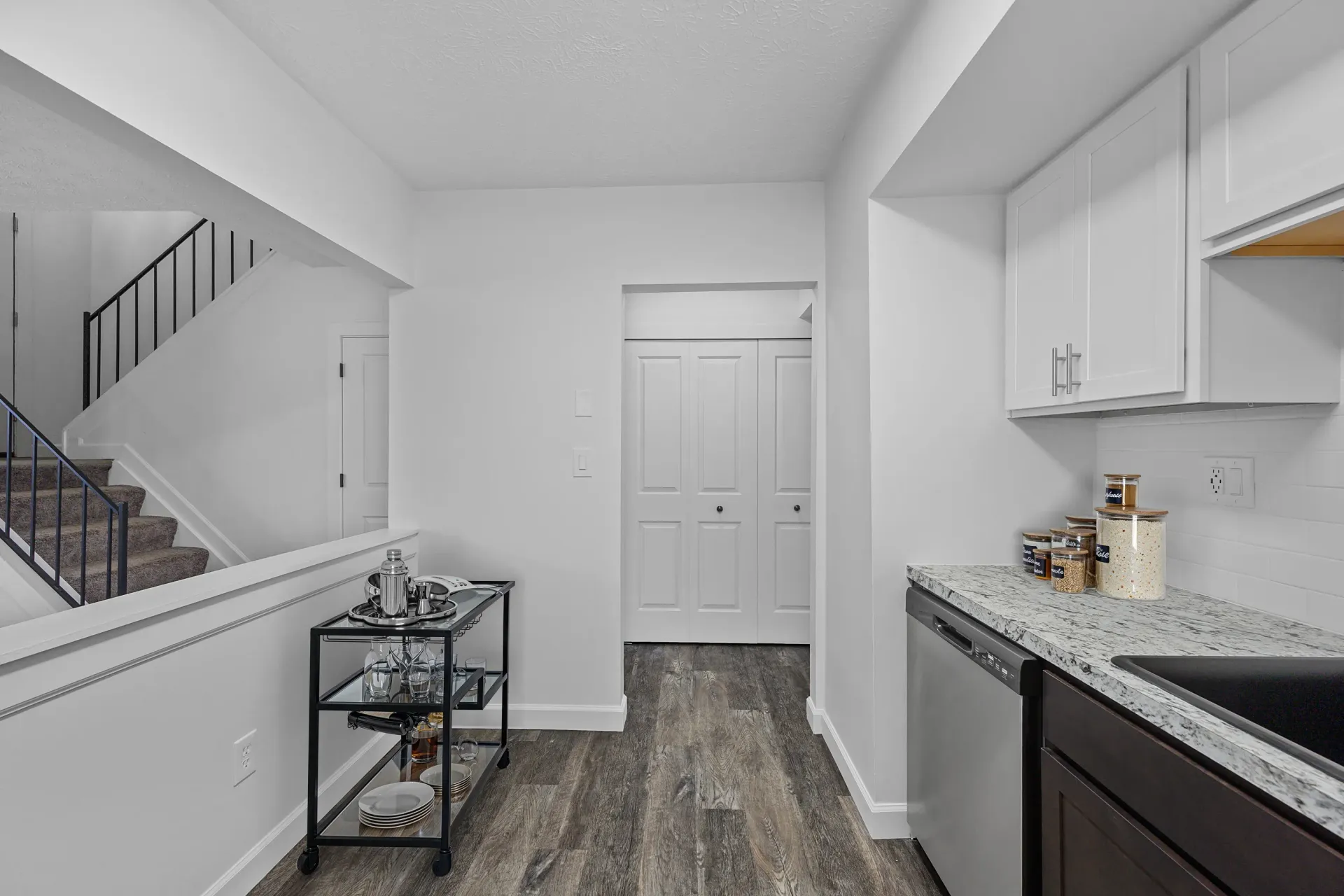 Open kitchen area with granite countertop, dishwasher, white cabinets, and stairs to the left.
