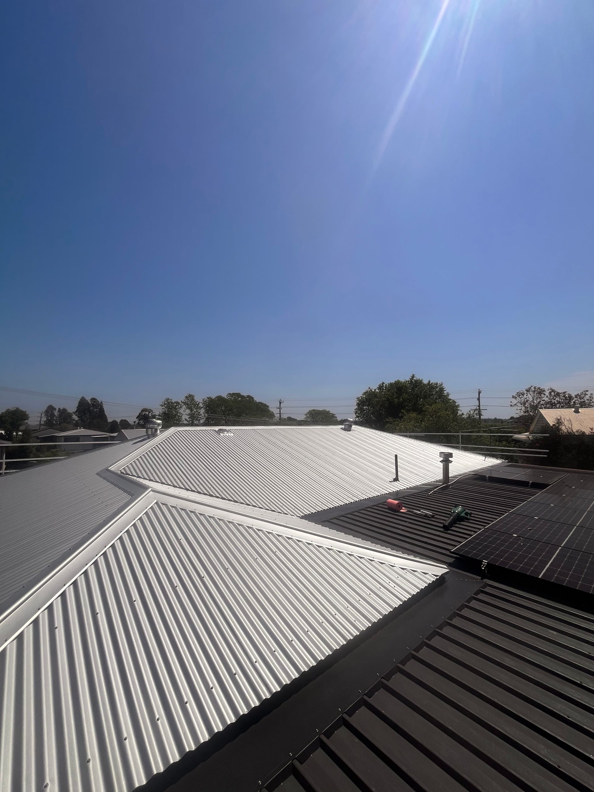 Bright sunlight over a building's corrugated metal roof with solar panels  — Eli Mcauley Constructions in Grafton, NSW