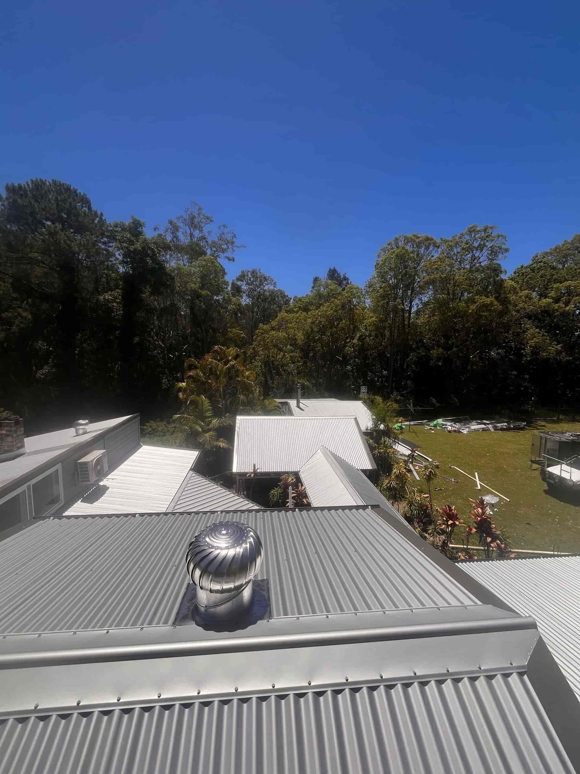 A view of a metal roof with a vent, trees in the background, under a blue sky— Eli Mcauley Constructions in Grafton, NSW