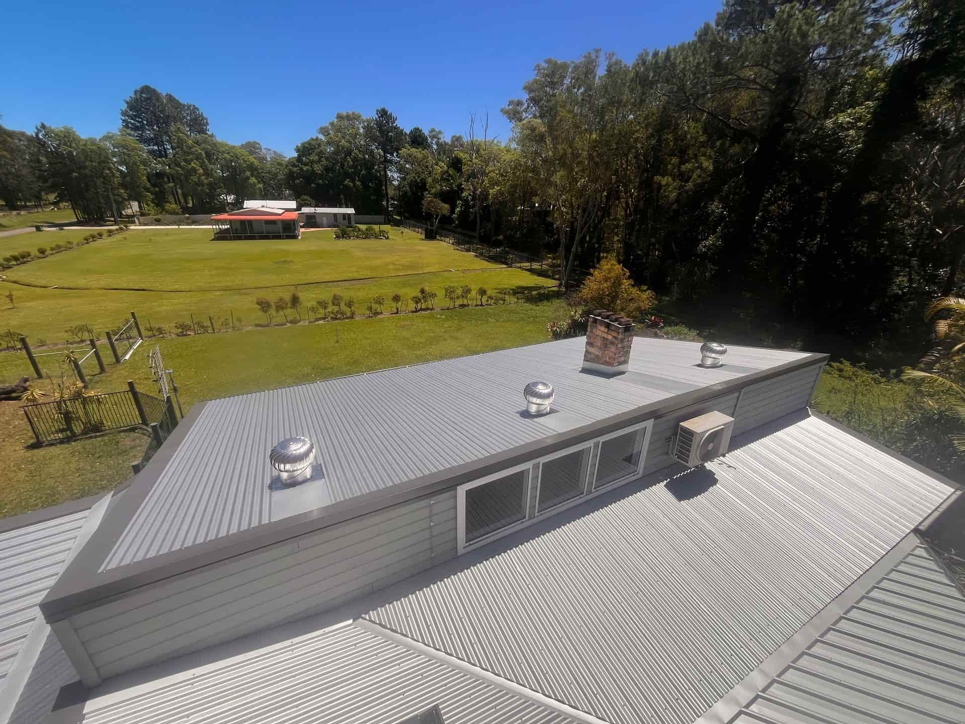 Metal roof on a building with a small wooden structure, trees in the background, clear blue sky— Eli Mcauley Constructions in Grafton, NSW
