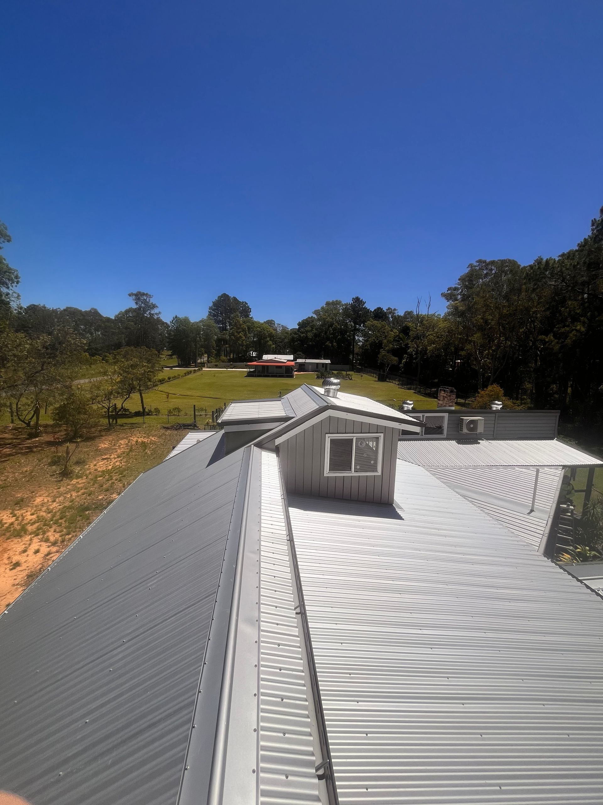 Gray metal roof with a small white structure and a distant red-roofed building on a sunny day— Eli Mcauley Constructions in Grafton, NSW