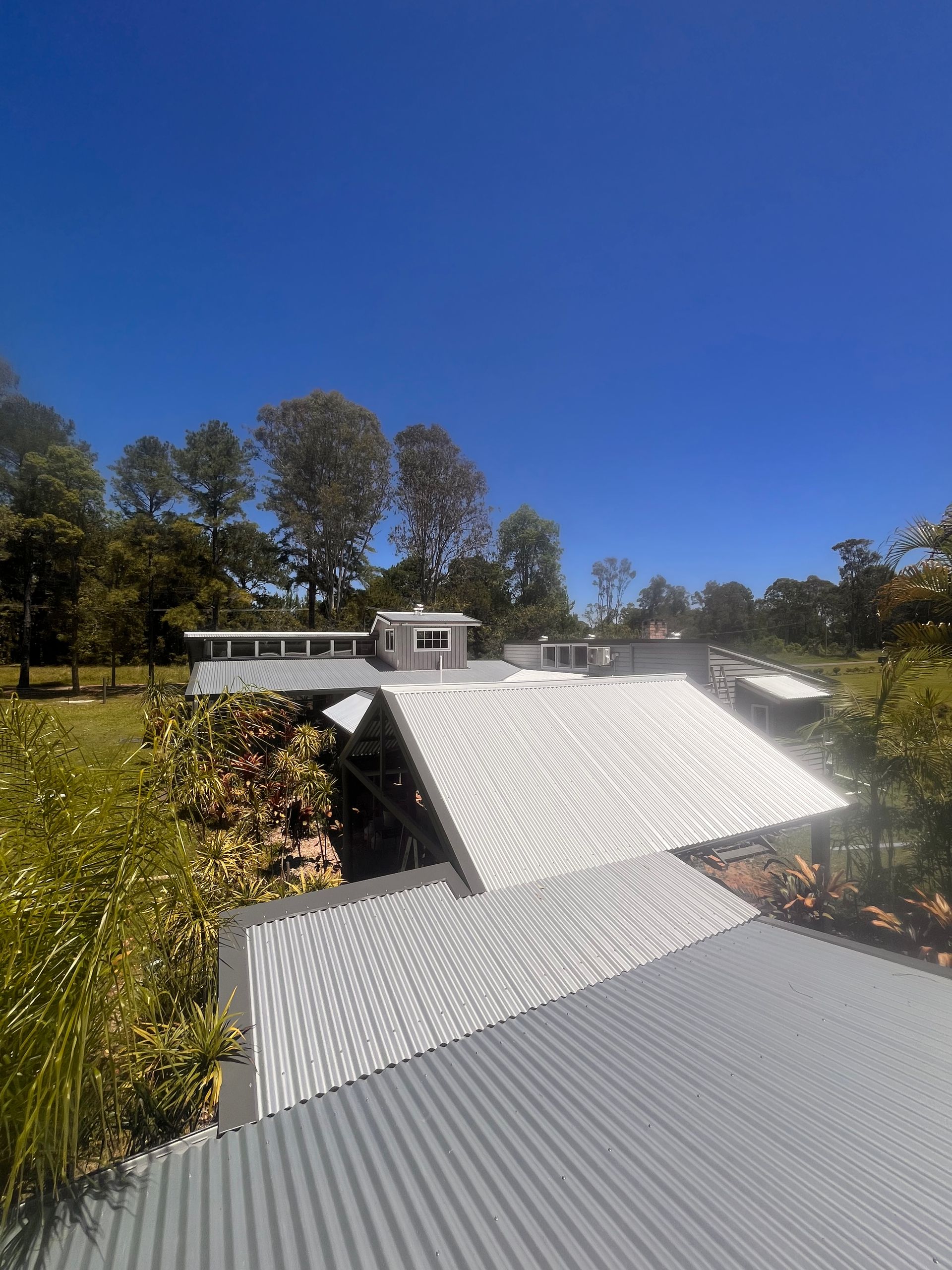 Grey metal roof of a house with trees and blue sky— Eli Mcauley Constructions in Grafton, NSW