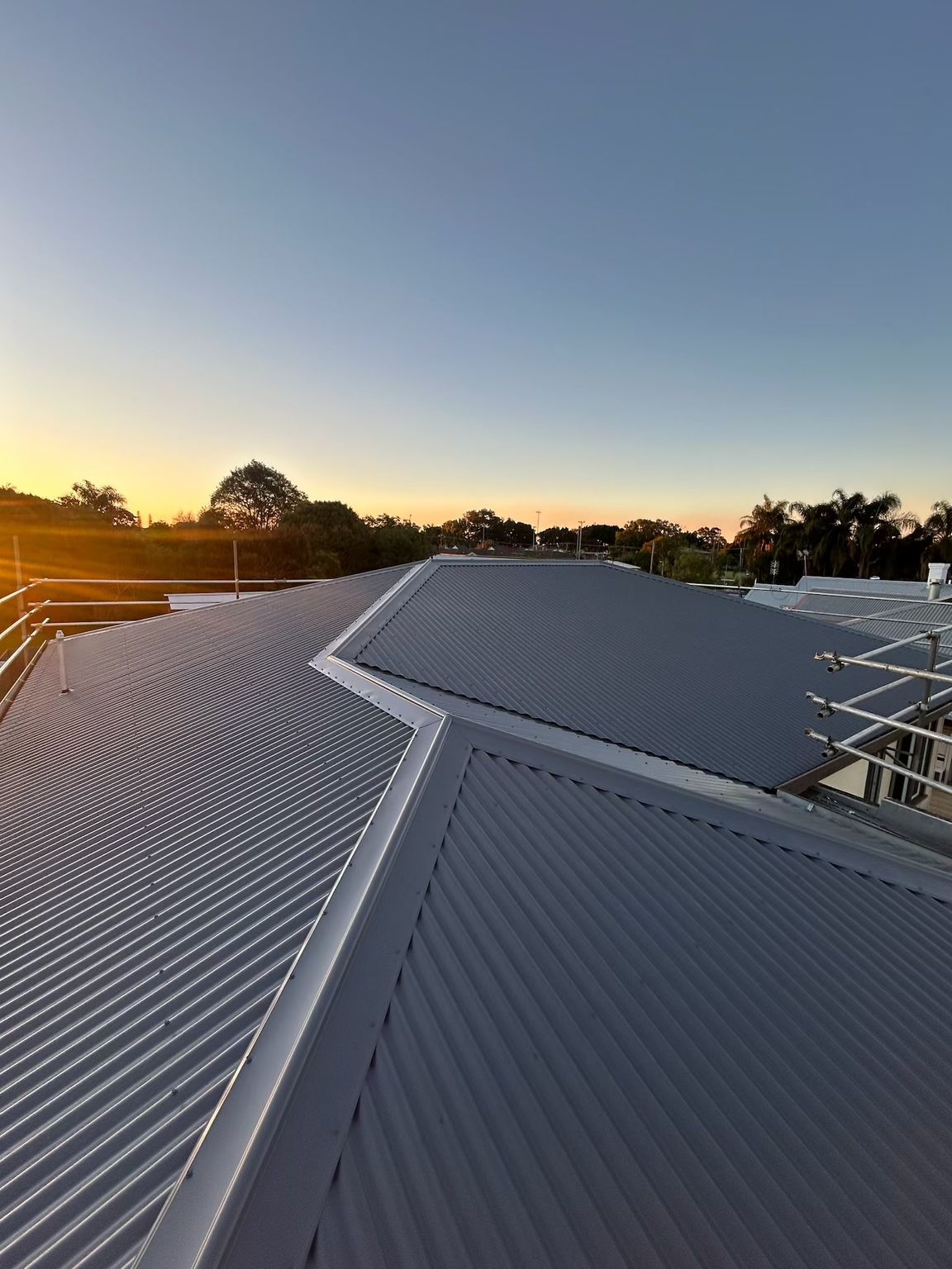 Metal roofs in a bright blue sky, with the sun shining, highlighting the corrugated patterns and different colors— Eli Mcauley Constructions in Grafton, NSW
