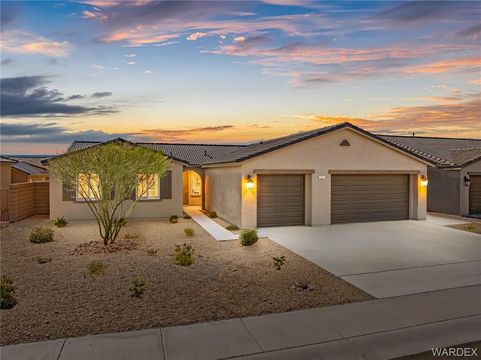 Single-story stucco house at dusk with lit entry, desert landscaping, and 4 car garage