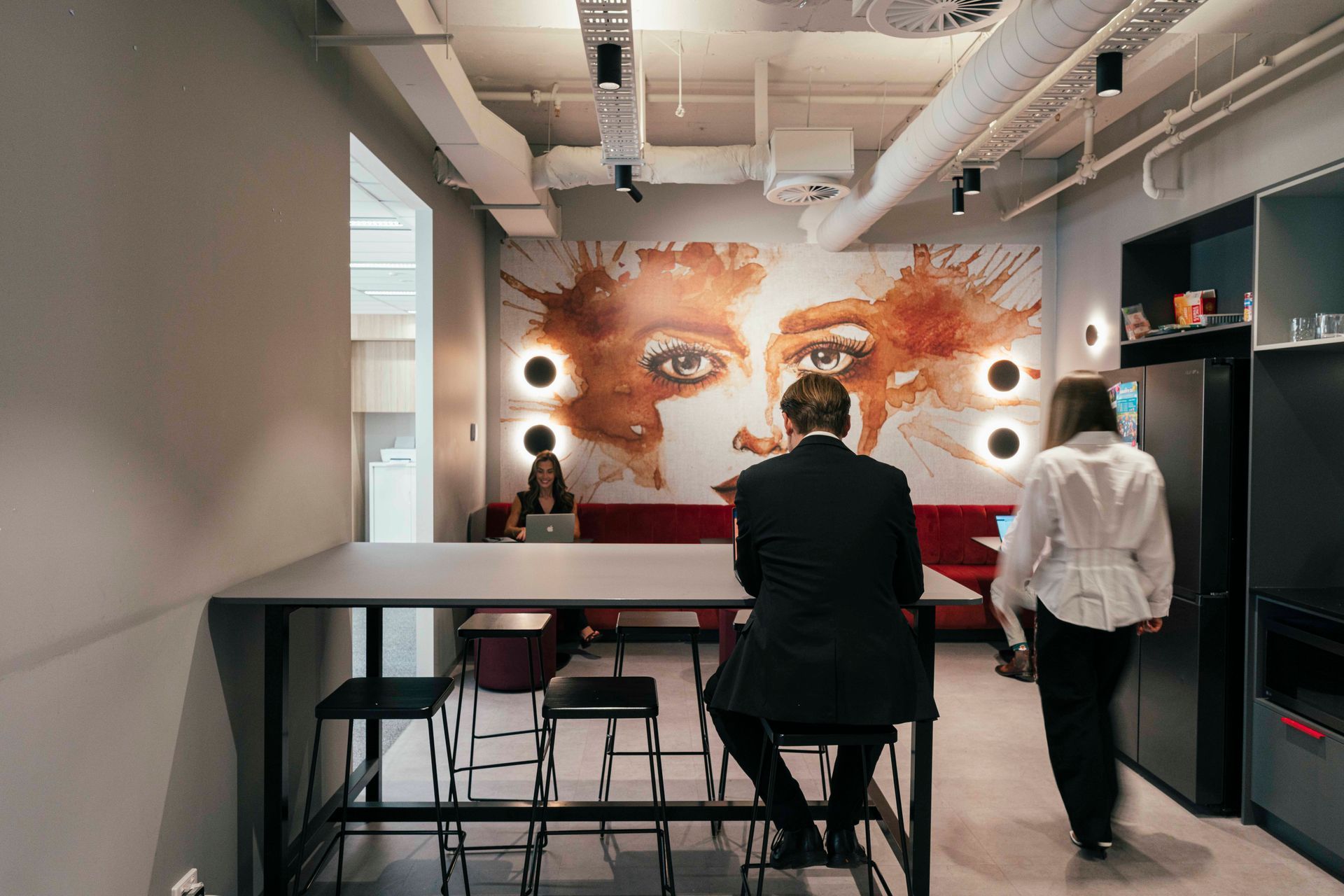 Two people in a modern studio facing a large illuminated mural of a face