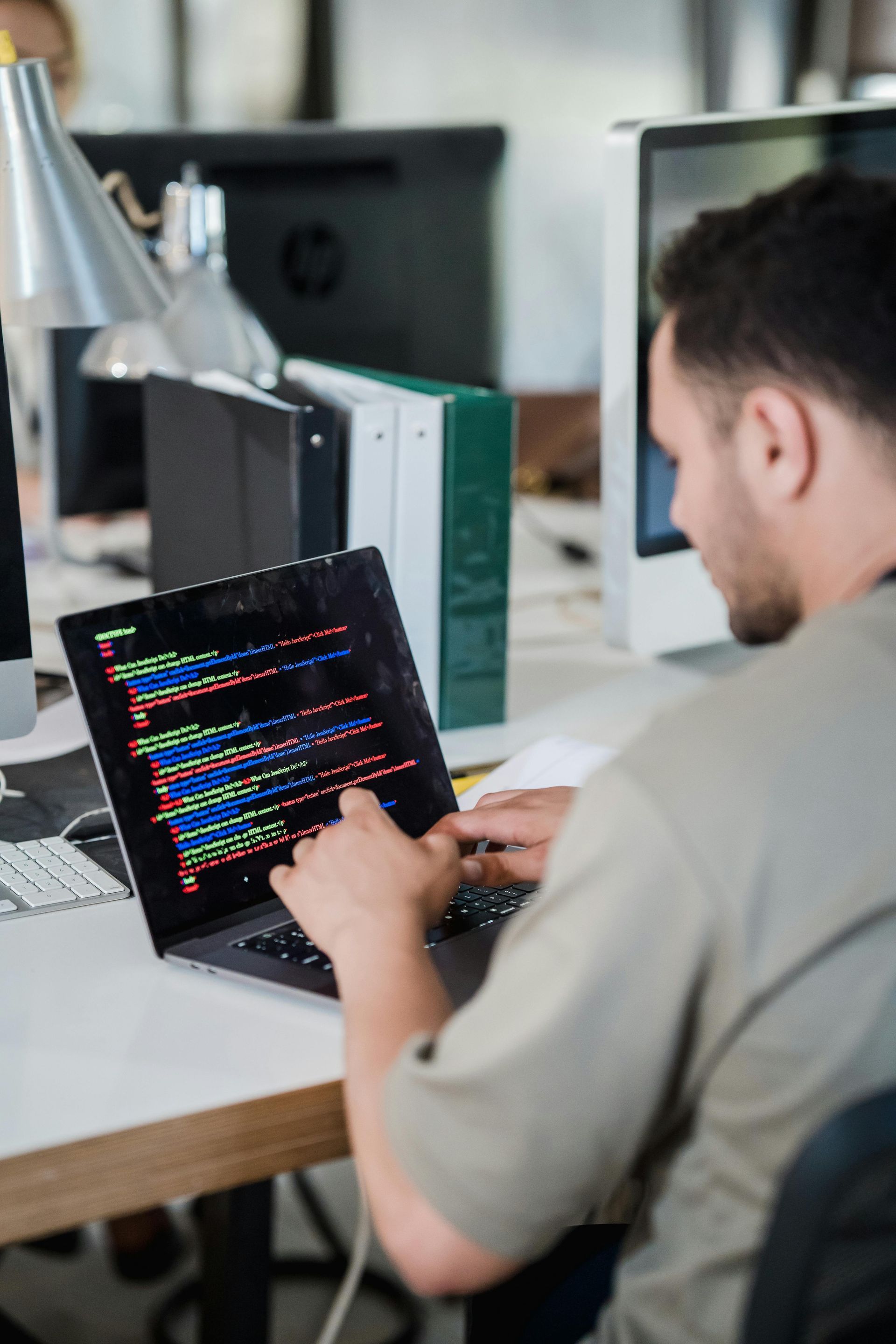 Person coding on a laptop at a desk in an office.