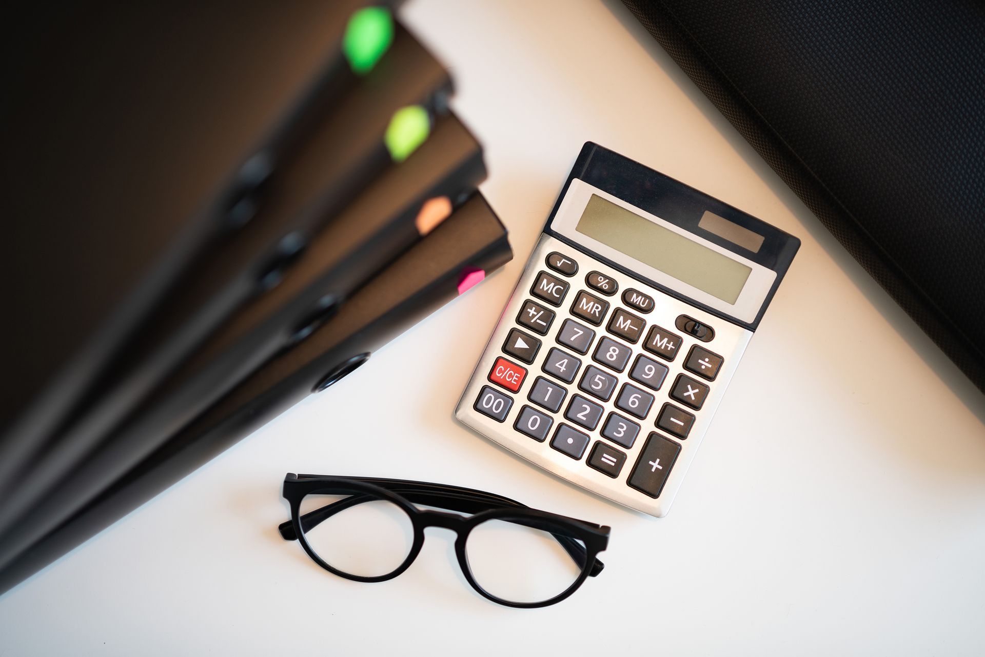 Calculator, black glasses, and colorful folders on a white desk