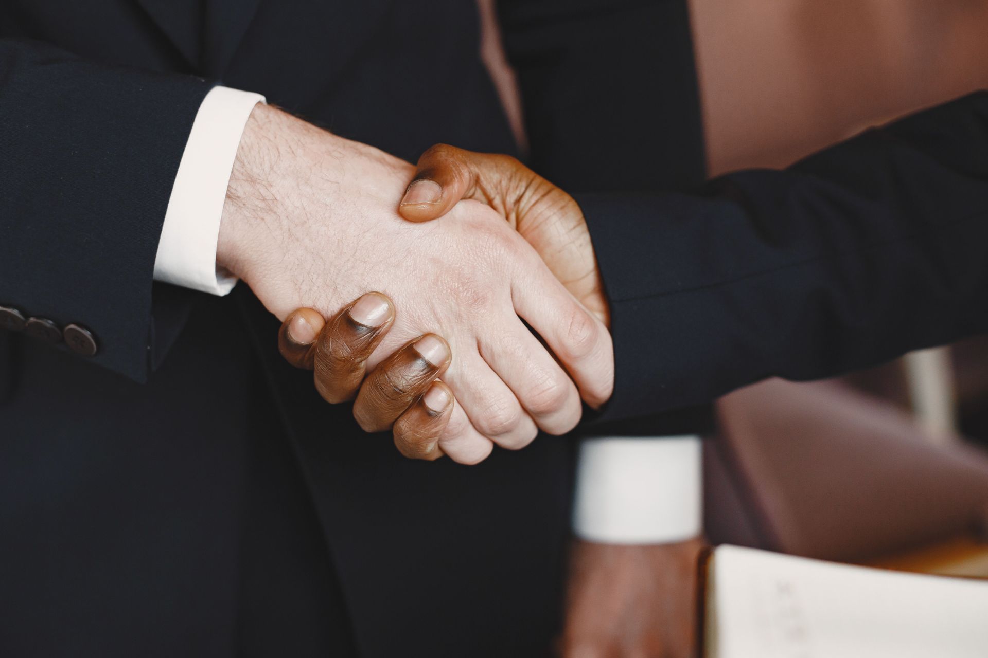 Two people in dark suits shaking hands in a formal setting