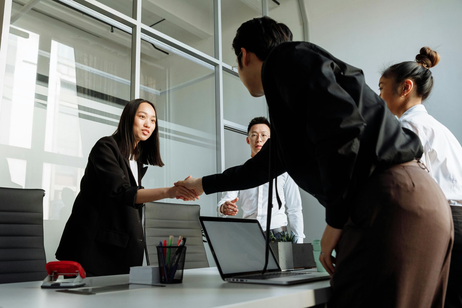 Coworkers shaking hands in a bright office meeting room with laptops on the table
