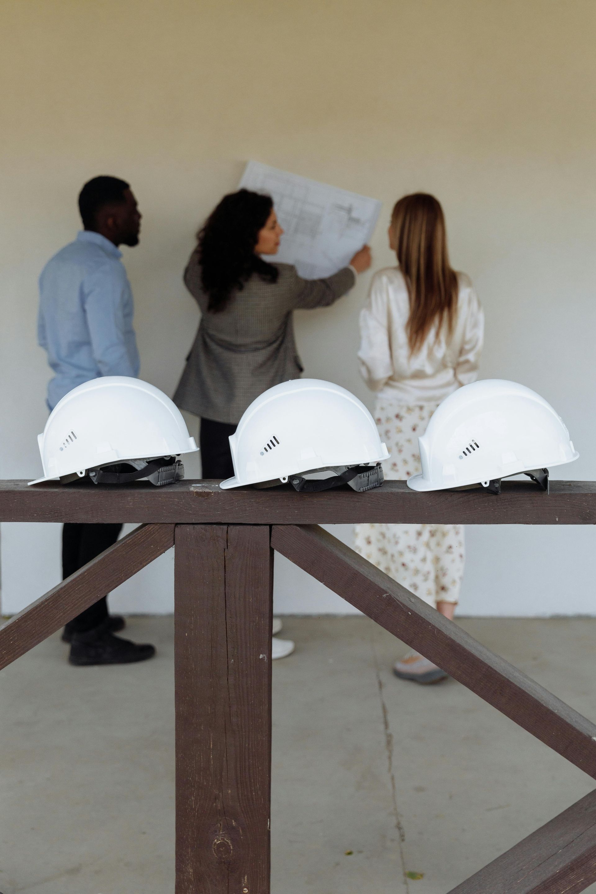 Three people review a map on a wall under a covered outdoor walkway beside white hard hats.