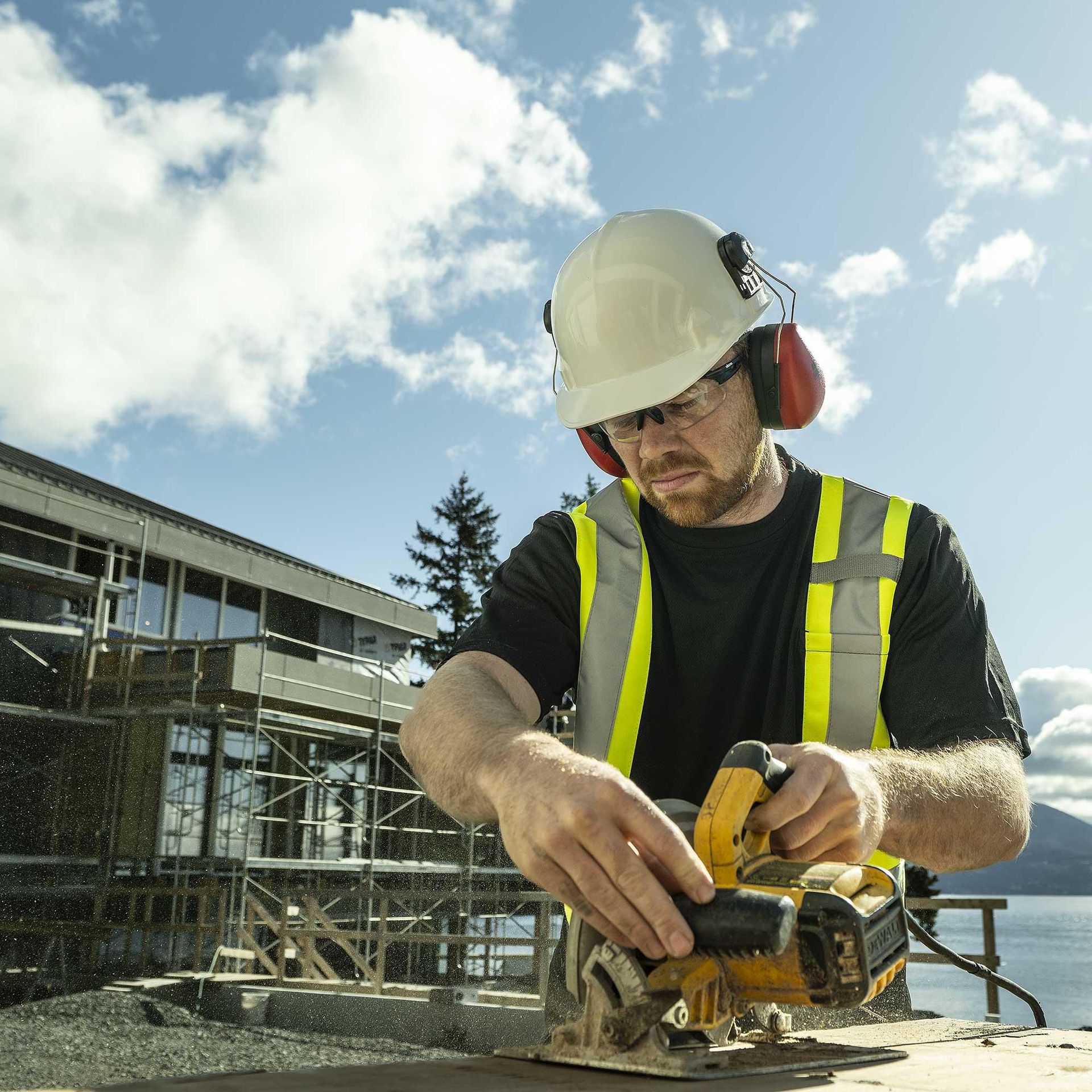 Construction worker in hard hat and safety vest using a circular saw at an outdoor building site