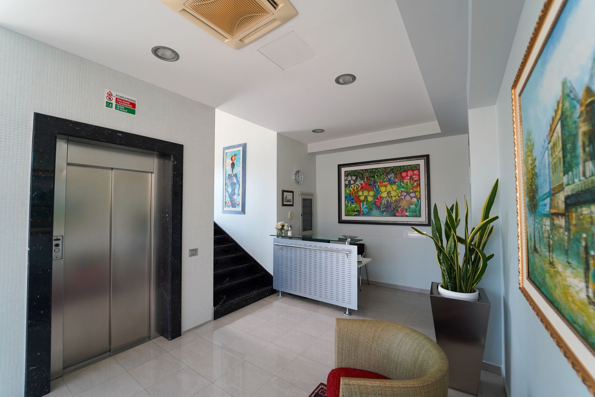 Hall moderna con ascensore, scala, reception e colorati quadri alle pareti.